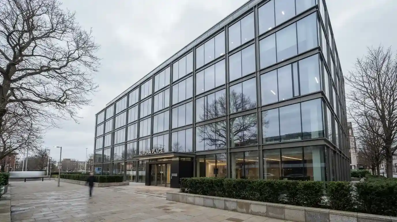 Edificio moderno de oficinas con grandes ventanales de cristal reflejando el cielo, visto desde una calle peatonal.