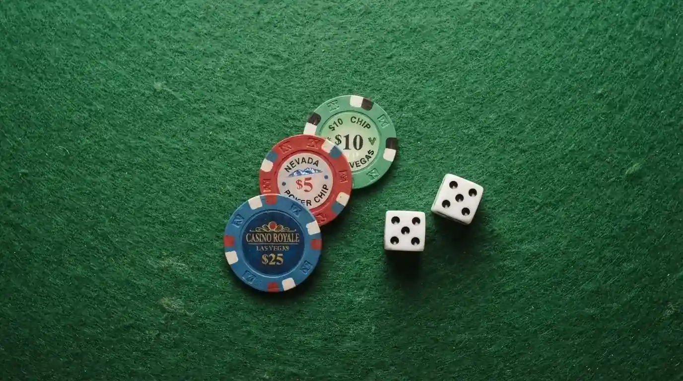 Vista cenital de fichas de casino y dados sobre una mesa de fieltro verde bajo luz suave.