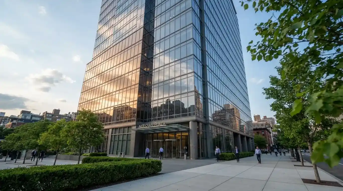 Un edificio de oficinas con fachada de cristal reflejando nubes, fotografiado desde una acera ancha por la tarde.